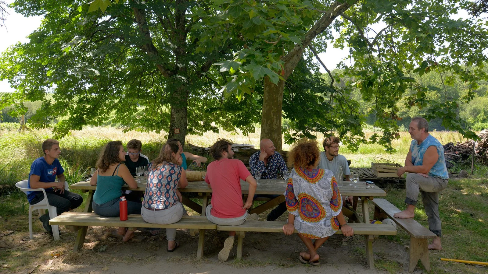 De longues tables sous les arbres, du monde attablé pendant la fête de Courtey
